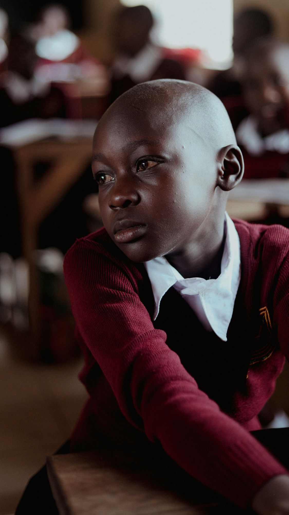 A student in a maroon school uniform looking out of a classroom window